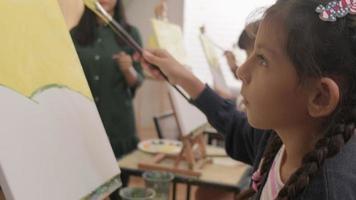 une petite fille se concentre sur la peinture acrylique couleur sur toile avec des enfants multiraciaux dans une classe d'art, l'apprentissage créatif avec des talents et des compétences dans l'enseignement en studio de l'école primaire. video