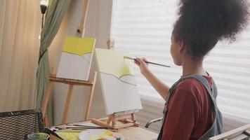 une jeune fille afro-américaine se concentre sur la peinture acrylique couleur sur toile avec un pinceau dans la salle de classe d'art, l'apprentissage créatif avec des talents et des compétences dans l'enseignement en studio à l'école primaire. video