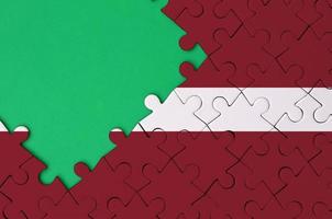 Latvia flag  is depicted on a completed jigsaw puzzle with free green copy space on the left side photo