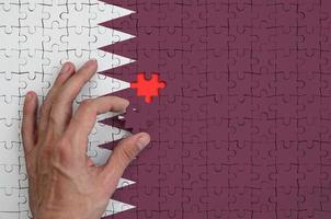 Qatar flag  is depicted on a puzzle, which the man's hand completes to fold photo