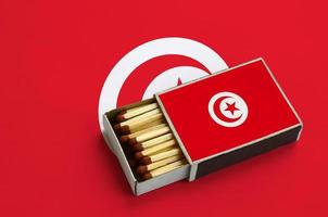 Tunisia flag  is shown in an open matchbox, which is filled with matches and lies on a large flag photo