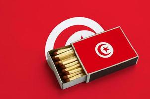 Tunisia flag  is shown in an open matchbox, which is filled with matches and lies on a large flag photo