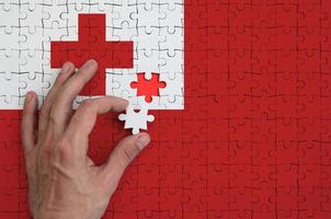 Tonga flag  is depicted on a puzzle, which the man's hand completes to fold photo