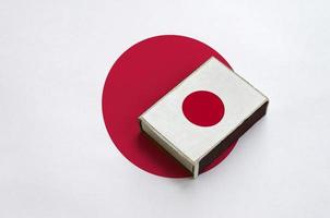 Japan flag  is pictured on a matchbox that lies on a large flag photo