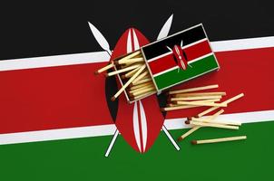 Kenya flag  is shown on an open matchbox, from which several matches fall and lies on a large flag photo