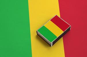 Mali flag  is pictured on a matchbox that lies on a large flag photo