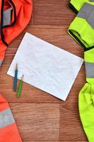una hoja de papel arrugada con dos lápices rodeada de uniformes de trabajo verdes y naranjas foto