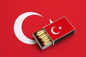 Turkey flag  is shown in an open matchbox, which is filled with matches and lies on a large flag photo