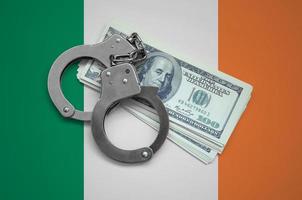 Ireland flag  with handcuffs and a bundle of dollars. Currency corruption in the country. Financial crimes photo