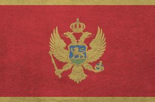 Montenegro flag depicted in bright paint colors on old relief plastering wall. Textured banner on rough background photo