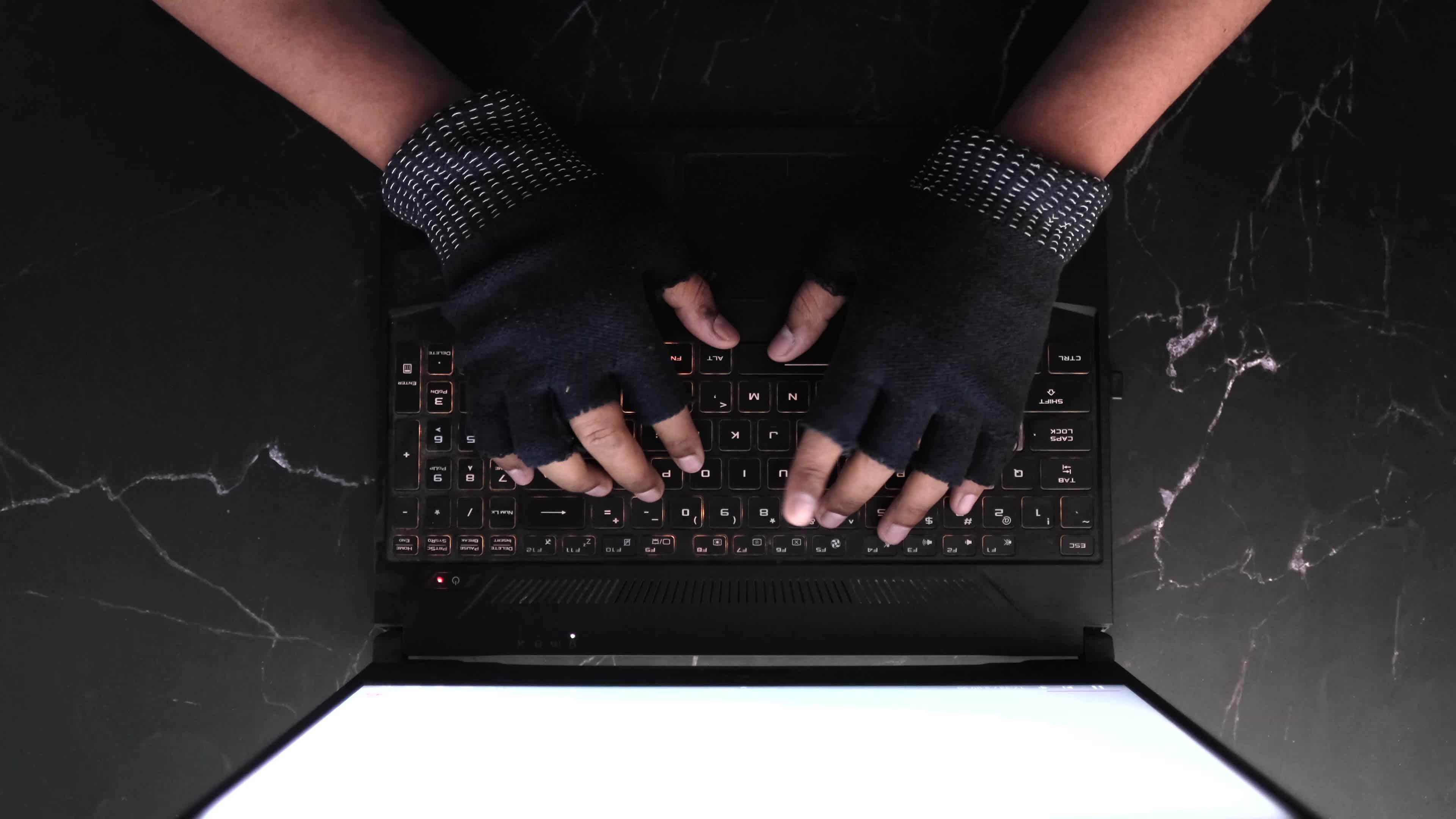 Overhead view of hands in fingerless gloves typing on a black laptop