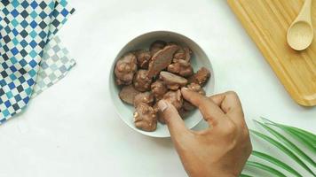 Hand enters frame to bowl of chocolate peanut cluster candies in a white bowl on a table with cutting board cloth napkin and plant video