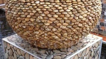 a fonte do jardim é feita de uma jarra com várias contas de pedra. Linda água corrente na superfície da textura da rocha. video