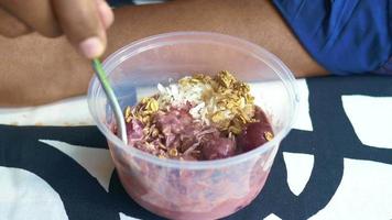 Using a spoon to eat smoothie bowl in plastic to go container video