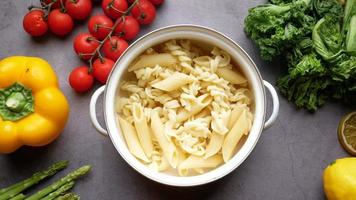 Sauce pan of mixed pasta on table with tomatoes peppers asparagus and greens video