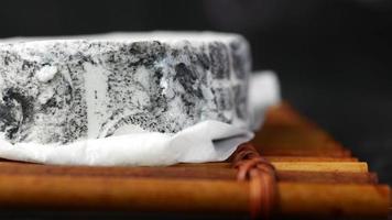Wheel of soft white cheese with dark gray marbling on wooden board video
