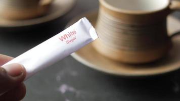 Paper packet of white granulated sugar with coffee mug in background video