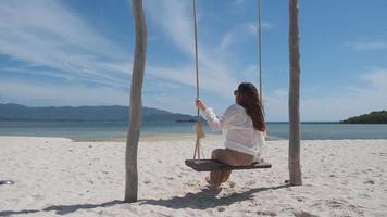 jong Aziatisch vrouw ontspannende Aan schommel strand zand in de mooi zee eiland achtergrond, vakantie concept video