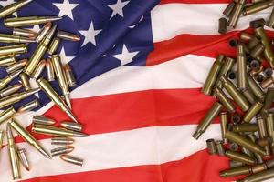 Many yellow 9mm and 5.56mm bullets and cartridges on United States flag. Concept of gun trafficking on USA territory or shooting range photo