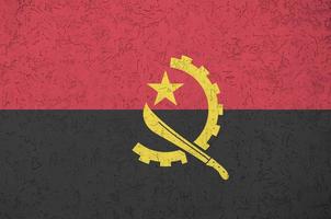 Angola flag depicted in bright paint colors on old relief plastering wall. Textured banner on rough background photo