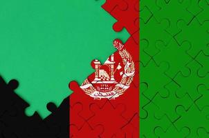 Afghanistan flag is depicted on a completed jigsaw puzzle with free green copy space on the left side photo