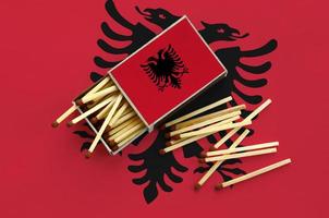 Albania flag  is shown on an open matchbox, from which several matches fall and lies on a large flag photo