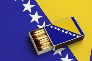 Bosnia and Herzegovina flag  is shown in an open matchbox, which is filled with matches and lies on a large flag photo