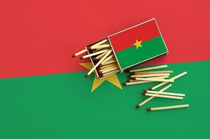 la bandera de burkina faso se muestra en una caja de cerillas abierta, de la que caen varias cerillas y se encuentra en una bandera grande foto