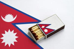 Nepal flag  is shown in an open matchbox, which is filled with matches and lies on a large flag photo