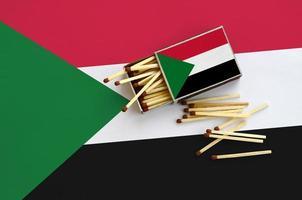 Sudan flag  is shown on an open matchbox, from which several matches fall and lies on a large flag photo