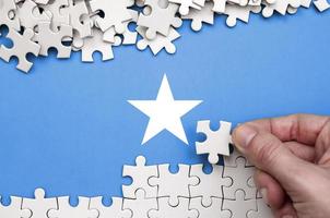 Somalia flag  is depicted on a table on which the human hand folds a puzzle of white color photo