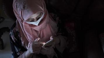 mulher de hijab e máscara facial usa um telefone inteligente em um quarto escuro video