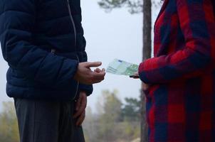 Girl transfers euro bills to the hands of a young guy in forest. Concept of robbery or illegal deal transaction photo