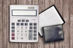 Office flat lay composition with calculator, address book and black purse on brown wooden table background with top view. Accountant paperwork concept photo