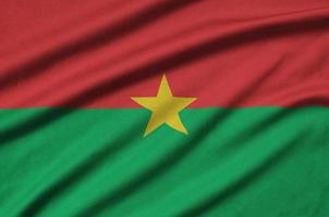 Burkina Faso flag  is depicted on a sports cloth fabric with many folds. Sport team banner photo