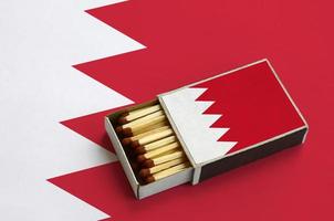 Bahrain flag  is shown in an open matchbox, which is filled with matches and lies on a large flag photo