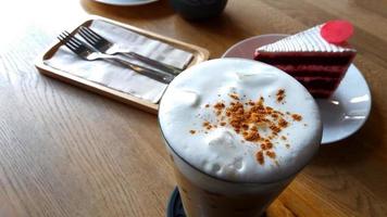 Closeup glass of Iced latte coffee, red  Raspberry red velvet cake with spoon and fork for eating on brown wooden table with copy space. Cold drinking and refreshments with dessert on wood background. photo