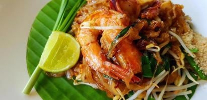 Close up stir fried with rice noodle, river prawn or shrimp, bean sprout, sliced chives and lime on banana leaf with copy space. Famous food in Thailand call Pad Thai. Selective focus technique. photo