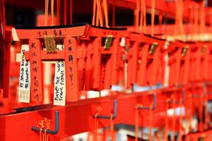 kyoto, japón - 25 de febrero de 2020 muchas pequeñas puertas torii colgando de una percha de madera roja en el santuario fushimi inanari. la gente escribe bendiciones en amuletos y reza para que sea verdad. foto