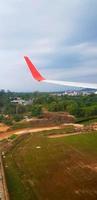 Red and gray or grey wing of plane with land, blue sky and white cloud background and copy space. Aerial view of airplane flying and going to destination. Top view of vehicle travel on high place. photo