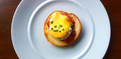 Flat lay of bread with poached egg, bacon and sweet sauce on top in dish. Top view of delicious meal of breakfast on white plate in American style. Food on table. photo