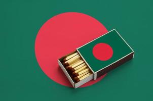 Bangladesh flag  is shown in an open matchbox, which is filled with matches and lies on a large flag photo