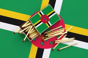 Dominica flag  is shown on an open matchbox, from which several matches fall and lies on a large flag photo