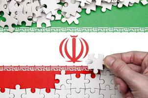 Iran flag  is depicted on a table on which the human hand folds a puzzle of white color photo