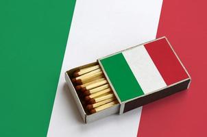 Italy flag  is shown in an open matchbox, which is filled with matches and lies on a large flag photo