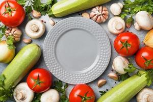 conjunto de diferentes verduras de temporada sobre un fondo de hormigón gris. tomate calabacín cebolla ajo champiñones perejil especias. espacio de copia de marco. foto