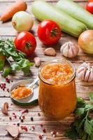 Homemade caviar from zucchini tomatoes and onions in a glass jar on a wooden background. Homemade production canning, canned stewed vegetable. photo