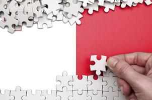 Malta flag  is depicted on a table on which the human hand folds a puzzle of white color photo