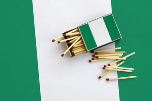 la bandera de nigeria se muestra en una caja de cerillas abierta, de la que caen varias cerillas y se encuentra en una bandera grande foto