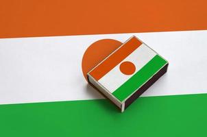 Niger flag  is pictured on a matchbox that lies on a large flag photo